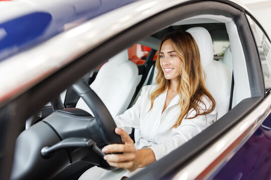 Fun cool driver woman customer buyer client in shirt hold put hand on steering wheel choose auto want buy new automobile in car showroom vehicle salon dealership store motor show indoor Sales concept