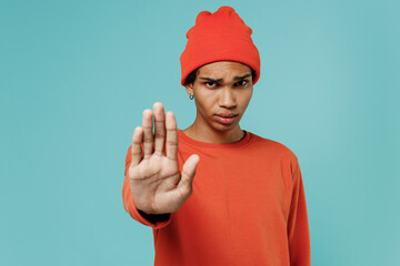 Young sad strict african american man 20s in orange shirt hat showing stop gesture with palm...