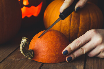 Female hands with a knife or miniature saw, carving a Halloween pumpkin Jack O'Lantern at home.