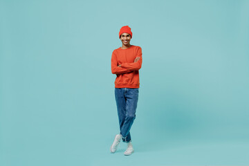 Fototapeta na wymiar Full body young smiling happy african american man 20s wear orange shirt hat stand hold hands crossed folded isolated on plain pastel light blue background studio portrait. People lifestyle concept