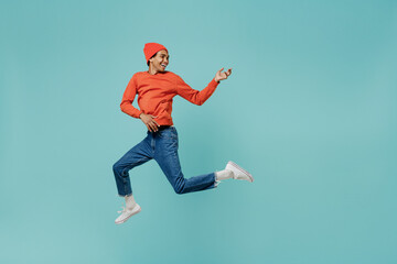 Naklejka na ściany i meble Full body young happy joyful satisfied african fun american man 20s in orange shirt hat jump high play guitar isolated on plain pastel light blue background studio portrait. People lifestyle concept.