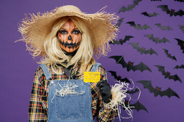 Young blonde woman with Halloween makeup mask in straw hat scarecrow costume hold in hand credit...