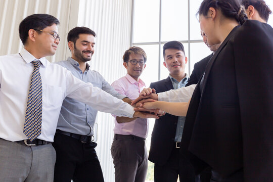 From Below Of Multiethnic Business Men And Women Stacking Hands Together While Standing In Office In Back Lit