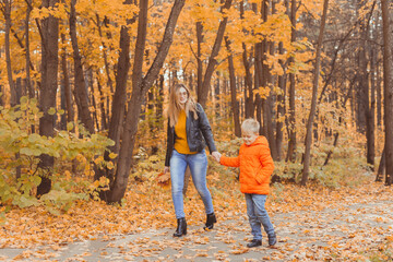 Fototapeta premium Mother and son walking in the fall park and enjoying the beautiful autumn nature. Season, single parent and children concept.