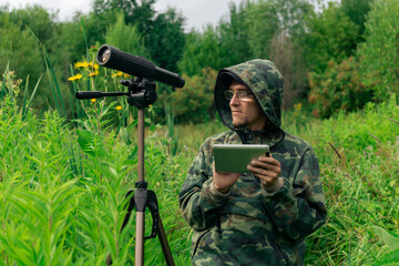 ornitologist looks at or writes down information on the tablet while standing among the tall grass...