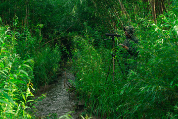 man birdwatcher makes field observation with a spotting scope among the thickets in a river valley