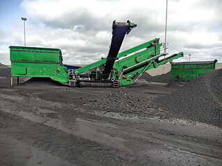 Mechanized loading of bulk cargo. Heaps of gravel on the dock and a harvester with transport belts. a loading harvester loads coal onto an offshore ship for delivery