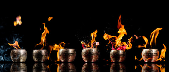 Potes dourados saindo fogo e liquido vermelho sobre espelho em fundo preto.