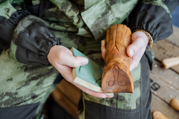 Obraz premium Man in a camouflage uniform processing a wooden product sitting on a light background.