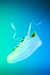 Fashion - white unisex sneakers shoe levitating on the neon blue and green background