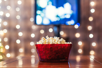 Christmas eve. Red bowl with popcorn on the table. Home cinema. Tv. Cropped, close up