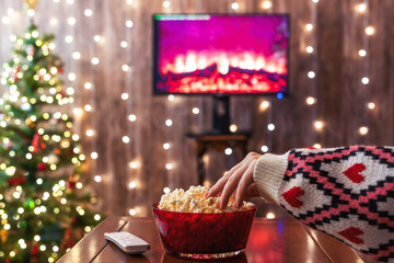 Christmas eve. Alone woman eating popcorn, watching tv, switching channels using remote control....