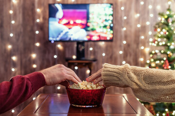 Christmas eve. Couple watching tv and eating popcorn. Home cinema. Cropped, close up