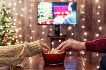 Christmas eve. Couple watching tv and eating popcorn. Home cinema. Cropped, close up - 458094701