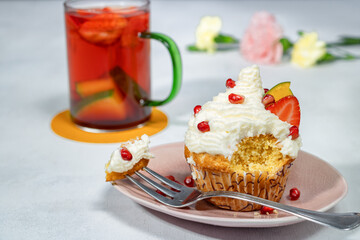Lemon cupcake with whipped cream and fruit. Fruit tea. Muffin with mango, strawberry, and pomegranate seeds.