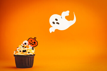 halloween cupcake decored with Jack O'Lantern and ghost colored sprinkles on a colorful orange...
