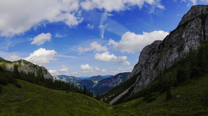 Fototapeta premium view to a deep valley with mountains and white clouds on the blue sky panorama