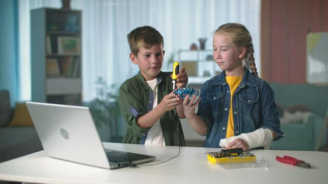 modern technologies, children with a screwdriver repair a mini quadcopter connected to laptop at the table at room