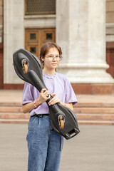 brunette teen with glasses with a skateboard on the streets of the city on a clear sunny day