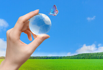 Glass globe of the planet Earth in human hand and flying butterfly