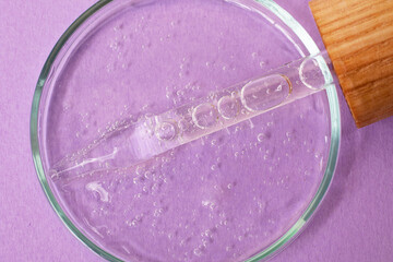 Pipette from dropper with wooden cover lies in the petri dish with cosmetics gel,closeup.Top view,liquid cosmetic,macro photography.Lilac banner with copy space.