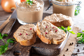 Chicken liver pate on bread and in a jar on rustic background