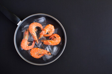 Top view of red shrimps in a frying pan on the black background.                 Copy space.