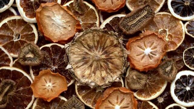 Background made of different dried fruits slices pineapple, persimmon, kiwifruit. Top view, table rotating.