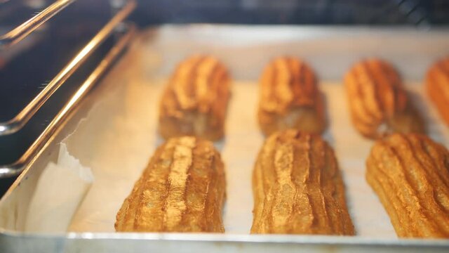 The final readiness of the French custard eclairs in the oven. Baked until golden brown. Dolly shot, close-up, DOF. Traditional national desserts concept