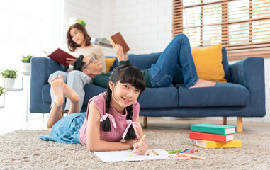 Relax Asian parent reading a book on sofa and daughter painting art in living room at home. panoramic background.