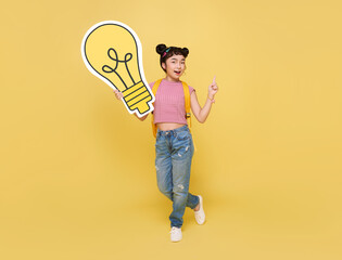 Happy Asian child student holding light bulb with schoolbag isolated on yellow background. idea thinking and creative concept.