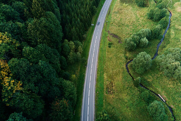 Cars moving on countryside road through mountains covered with pine tree forest, aerial view. Car...