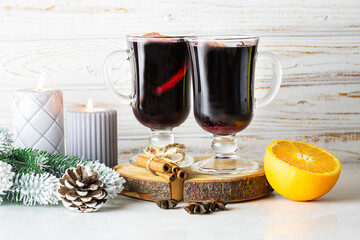 Aromatic hot mulled wine with oranges and spices on light rustic background with candles and Christmas decorations. Traditional winter alcoholic drink.