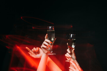Corporate party. Christmas celebration. Festive greeting. Holiday fun. Female hands holding glasses of champagne long exposure defocused red light isolated black.