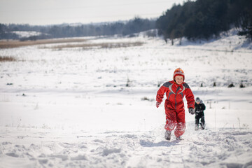 A boy in a ski suit on a snow mountain with a sled. The child is riding a sledge scooter . Active games on the street. Healthy lifestyle