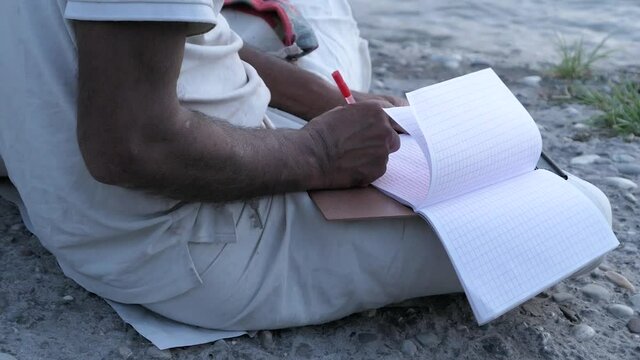 A monk writes down prayers in a notebook. The bank of the Ganges in the holy city of India.
