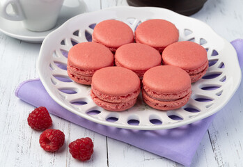 Berry macarons on a plate with coffee over wooden table