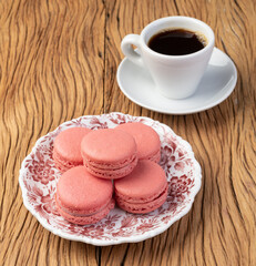Berry macarons on a plate with coffee over wooden table