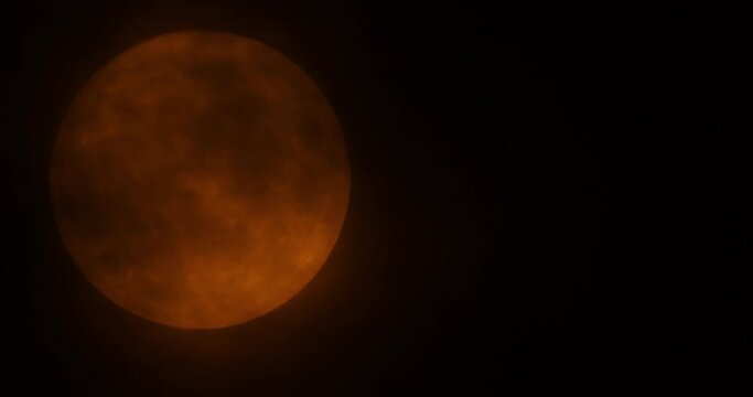 Orange rising moon by the bourgeois plan. The moon passes slowly through the clouds, the clouds blur the moon a little.