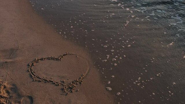 the sea wave washes away the heart drawn in the sand
