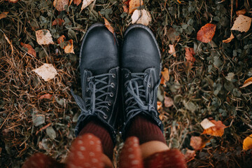 Legs of a girl in black boots and brown socks on a background of colorful autumn leaves