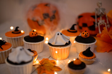 Halloween muffins with decorations in the form of ghosts, pumpkins and witch hats. A set of festive cupcakes and treats for a Halloween party.