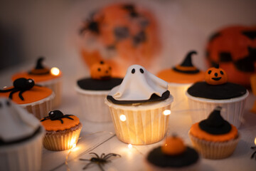 Halloween muffins with decorations in the form of ghosts, pumpkins and witch hats. A set of festive cupcakes and treats for a Halloween party.