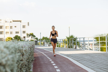 beautiful fitness girl in shorts and sports top running on the waterfront by the sea in sunny weather