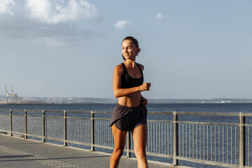 beautiful fitness girl in shorts and sports top runs on the waterfront by the sea during sunset