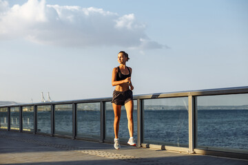 beautiful fitness girl in shorts and sports top runs on the waterfront by the sea during sunset