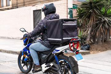 Food delivery driver with backpack on a motorcycle riding along a street.