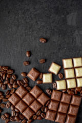 Pieces of milk and white chocolate with coffee beans on a dark background