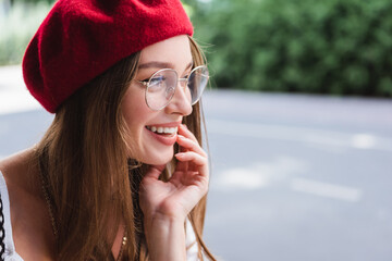 Fototapeta premium happy young woman in red beret and eyeglasses looking away outside