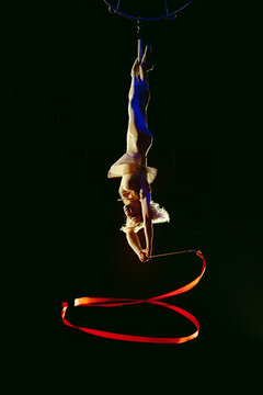 An aerial gymnast shows a performance with a ribbon in the circus arena.